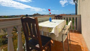 Ein Balkon mit Tisch und Stühlen, eine Vase mit einer Blume und Blick auf die Landschaft.