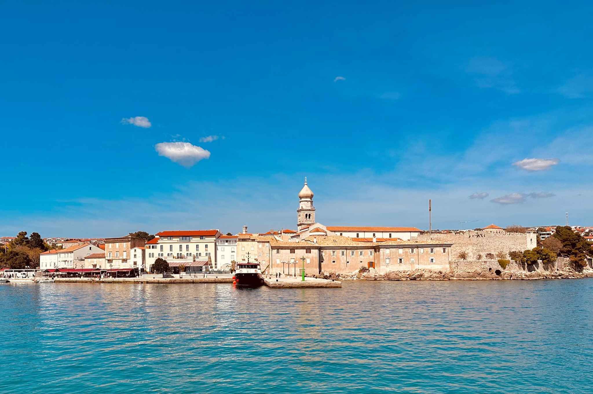 A waterfront cityscape with historic buildings, a prominent tower, and a calm sea.