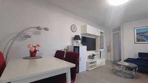 Ein modernes Wohnzimmer mit einem weißen Tisch, roten Stühlen, einem Fernseher und einem Bild an der Wand.