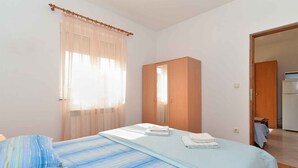 Une chambre avec deux lits, une armoire en bois et une salle de bain visible à travers une porte ouverte.