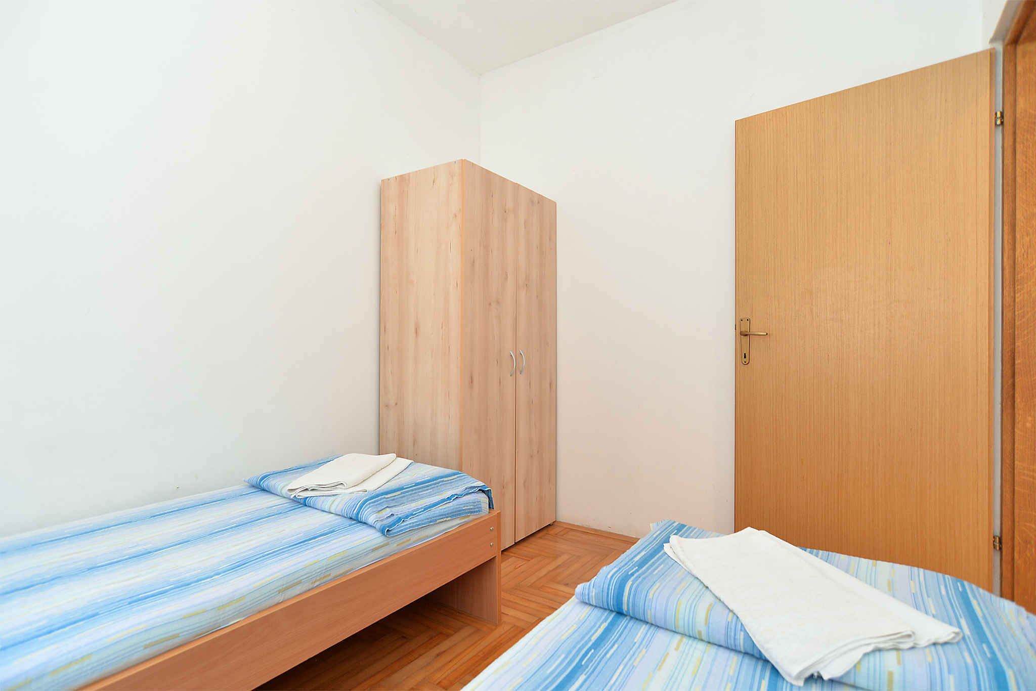 A small, single-occupancy room with a wooden wardrobe and a bed with striped bedding.