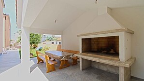 Une terrasse extérieure avec une table et des bancs en pierre, une cheminée en briques et une vue sur les bâtiments voisins.