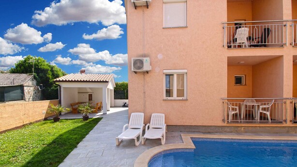 Un immeuble résidentiel doté d’une piscine, de deux chaises longues et d’un petit espace patio.