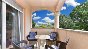 A balcony with a table and four chairs, a glass door, and a view of trees and sky. - Holiday apartment with air conditioning (Medulin)