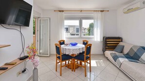 A living room with a sofa, a TV mounted on the wall, a dining table with chairs, and a window with curtains. - Holiday apartment with air conditioning (Medulin)