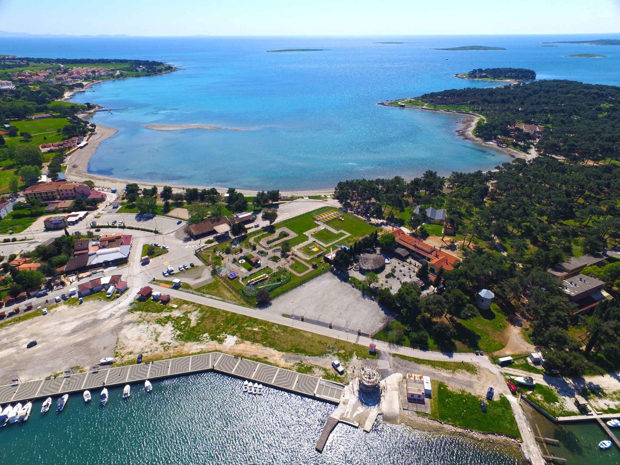 Vue aérienne d’une zone côtière comprenant un port de plaisance, un vaste champ et des immeubles résidentiels.