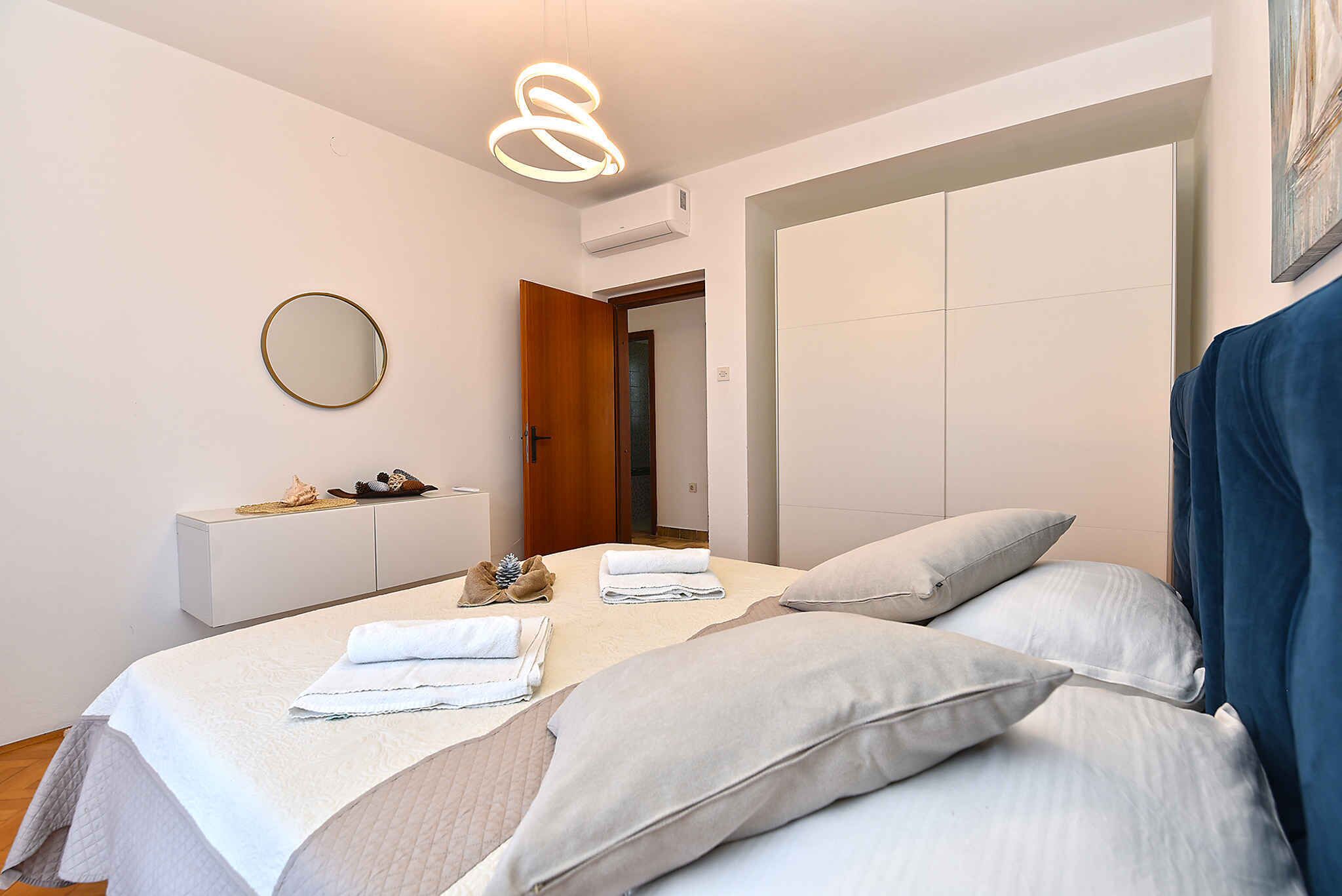A bedroom with a bed, pillows, a bedside table, a mirror, and a hanging light fixture.