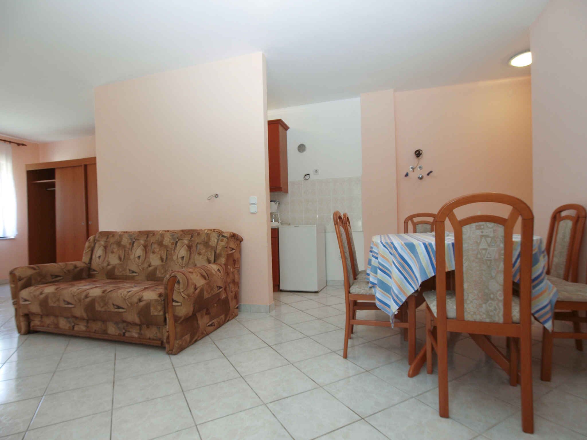 A living room with a sofa, a dining table with chairs, a kitchen area, and a door leading to another room.