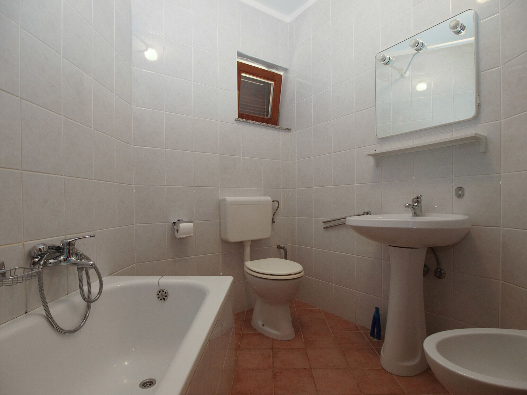 Ein Badezimmer mit Badewanne, Toilette, Waschbecken und einem kleinen Fenster.
