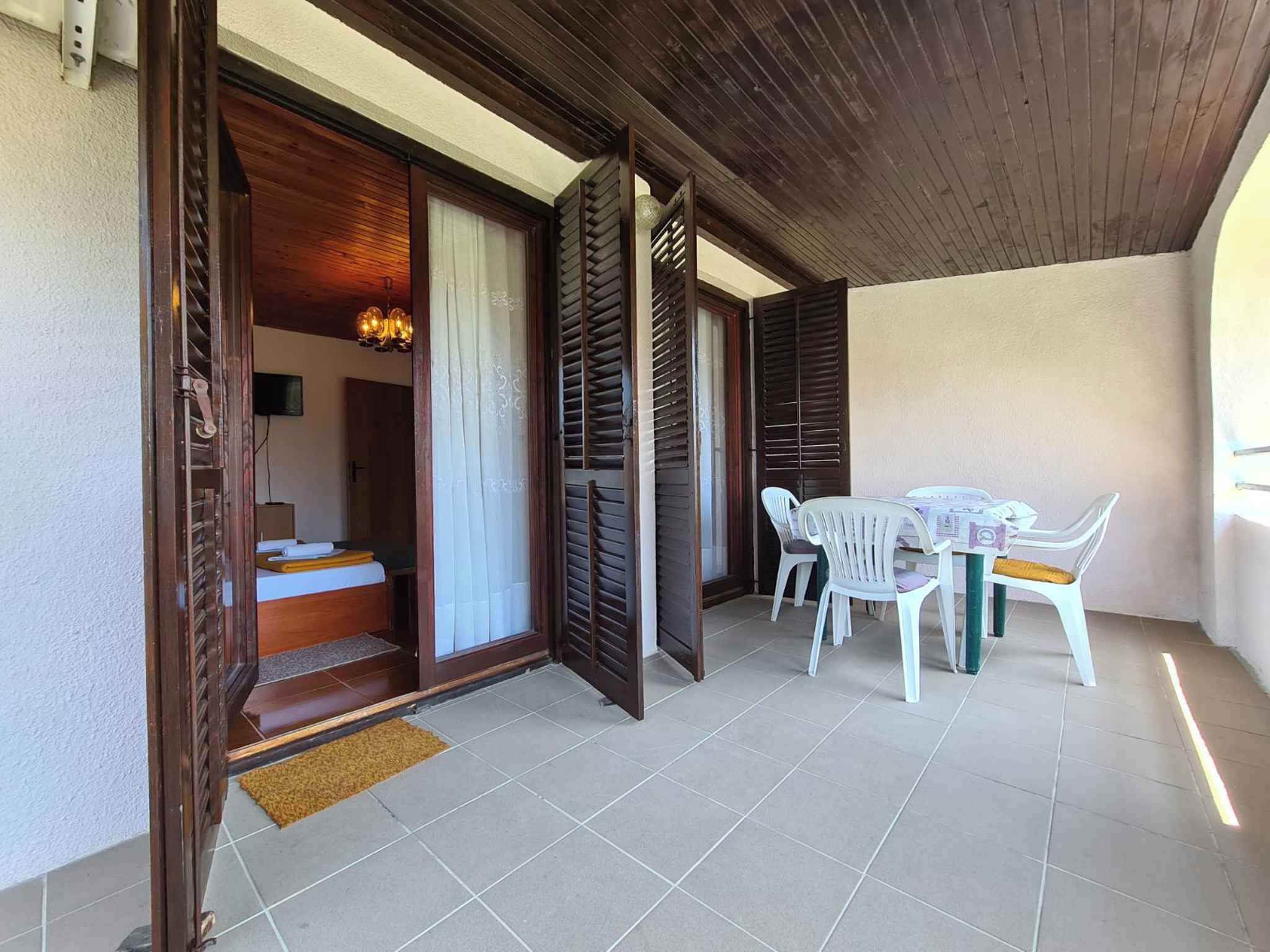 Un balcón con techo de madera, un comedor con sillas de plástico blanco y una cama con cabecera de madera.