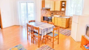 Une cuisine compacte équipée d’une cuisinière, d’un évier et de placards. On y trouve une table à manger avec des chaises, ainsi qu’un téléviseur posé sur un meuble.