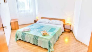 Un lit bien fait, recouvert d’une couvre-lit à carreaux verts et blancs, avec deux lampes de chevet et une tête de lit en bois.