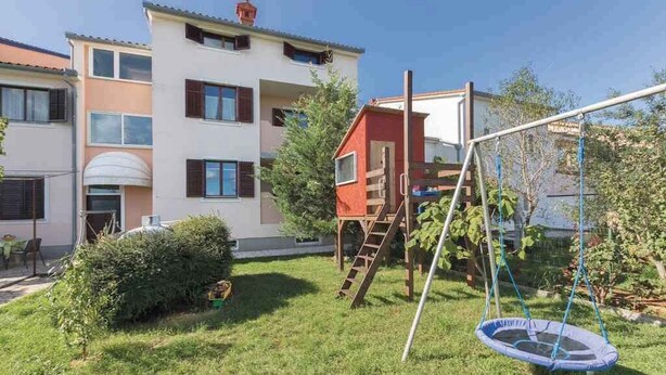 A residential building with a small backyard, a swing set, and a trampoline.