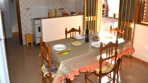 A dining area with a table set for four, chairs, a refrigerator, a sink, and a window with a view.