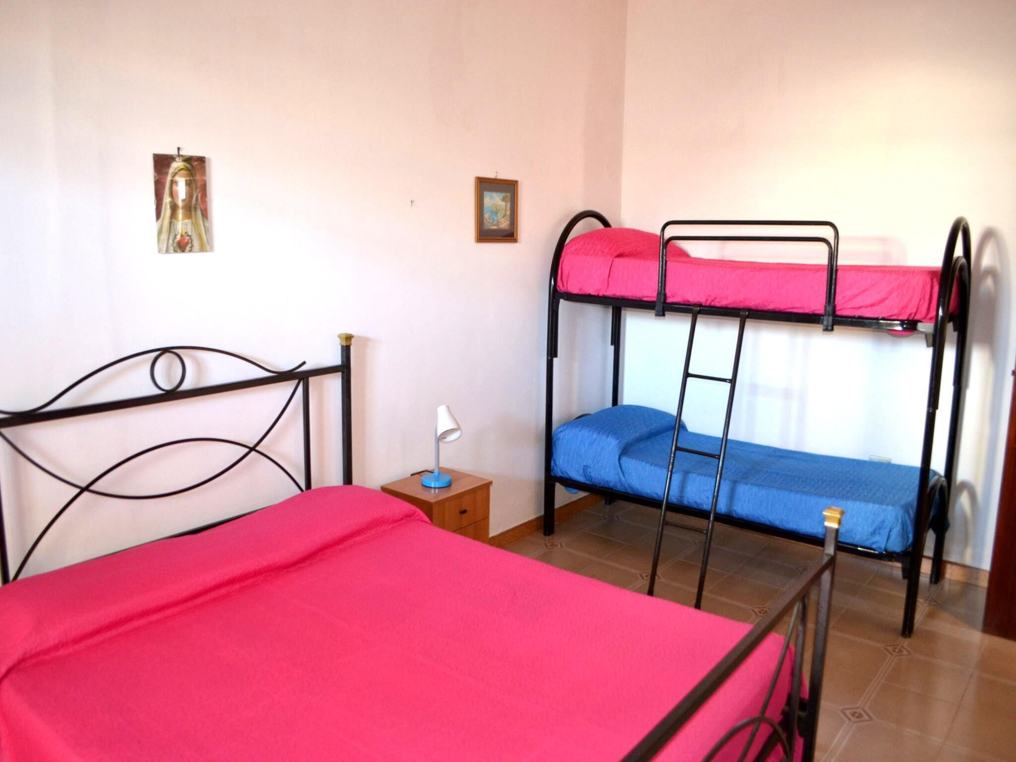 A room with bunk beds, a bedside table with a lamp, and two framed pictures on the wall.