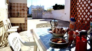 An outdoor dining area with a table set for two, a coffee pot, a bowl of bread, and condiments.