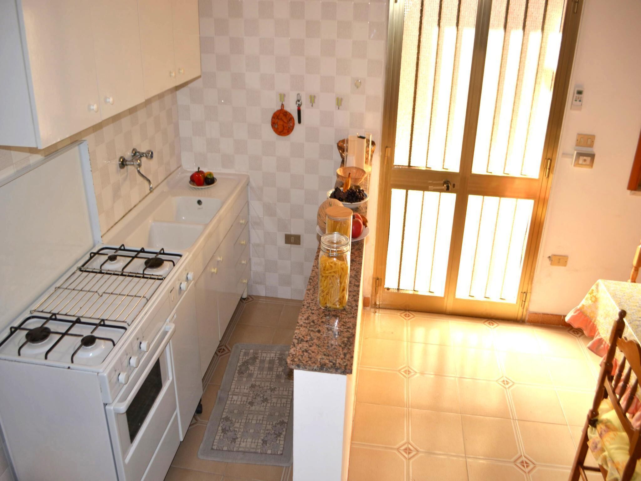 A compact kitchen with white cabinets, a gas stove, a sink, and a window with blinds.