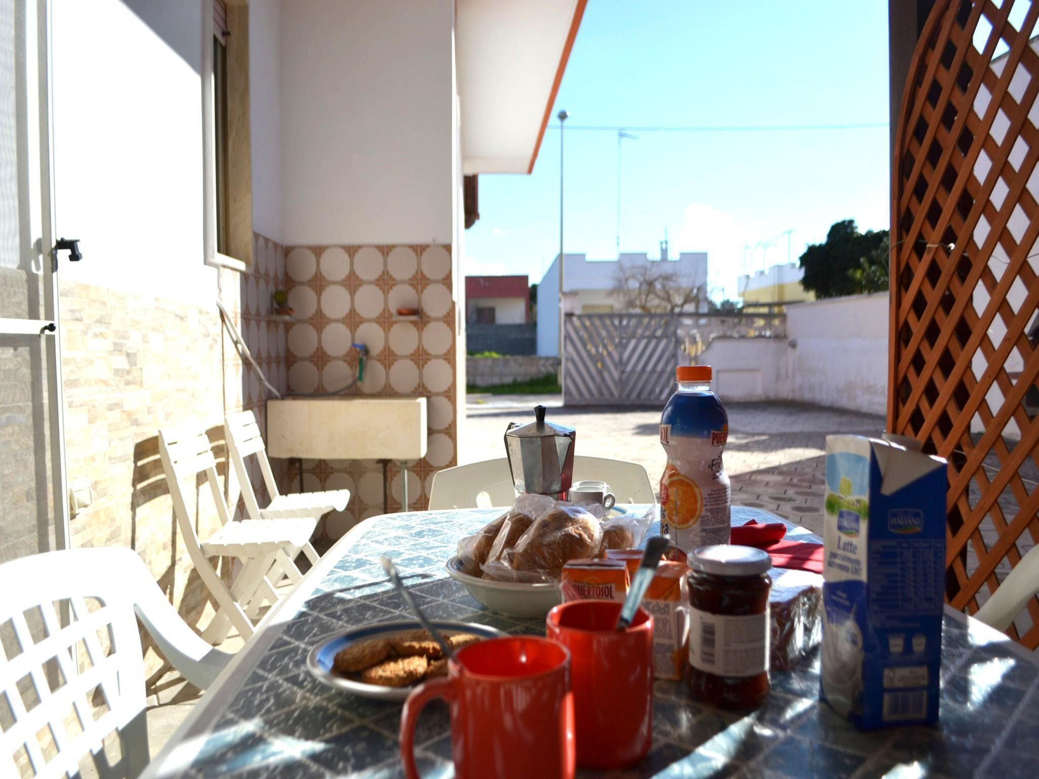 A table set with food and drinks, a chair, and a view of a building and gate in the background.