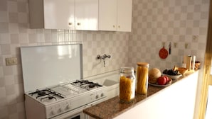 A kitchen with white cabinets, a gas stove, an oven, and a countertop with jars of pasta and fruits.