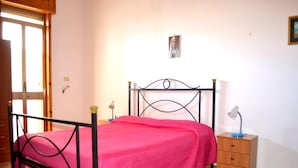 A bedroom with a bed, a nightstand, a lamp, a picture on the wall, and a window.