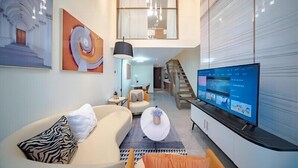 A modern living room with a sofa, a coffee table, a TV, and a staircase leading to an upper level. - Millenia Executive Apartment Guangzhou East Railway Station Zhujiang New Town Branch - Free Shuttle Bus to Canton Fair Complex During Canton Fair Period (Guangzhou)