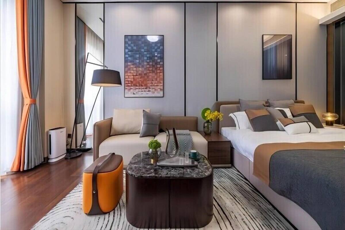 A modern hotel room with a sofa, a bed, a coffee table, and a painting on the wall.