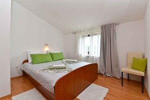 Ein Schlafzimmer mit einem hölzernen Bett, grünen Kissen, einer Nachttischlampe, einem Stuhl und einem Fenster mit Vorhängen.