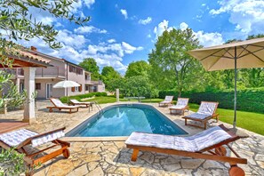 Ein Swimmingpool mit Liegestühlen und einem Sonnenschirm, umgeben von Steinböden und Grünpflanzen.