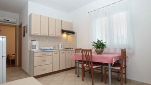 A compact kitchen with a dining area, featuring a table with chairs, a potted plant, and a window with sheer curtains. - Holiday apartment with air conditioning (Fažana)