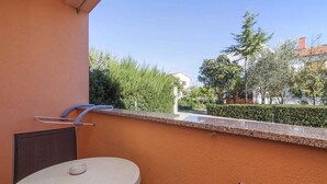 A balcony with a round table and chairs, a metal railing, and a view of greenery and buildings. - Holiday apartment with air conditioning (Fažana)