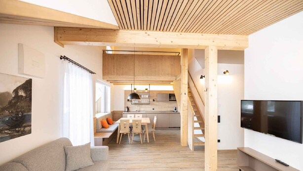 A modern interior with a wooden ceiling, a sofa, a dining table, a TV, and a kitchen area.