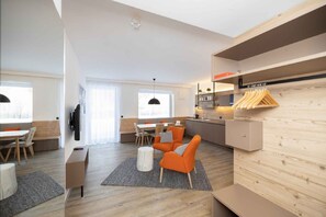 A modern hotel room with a wooden floor, a dining area with a table and chairs, a sofa, a TV, and a kitchen area with a sink and wooden shelves. - Studio with wellness area (Hinterstoder)