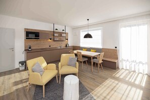 A modern kitchen with built-in appliances, a dining area with wooden furniture, and a large window providing natural light. - Studio with wellness area (Hinterstoder)