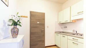 A modern kitchen with white cabinets, a wooden door, and a vase with flowers on a counter. - Holiday apartment with air conditioning (Lignano)