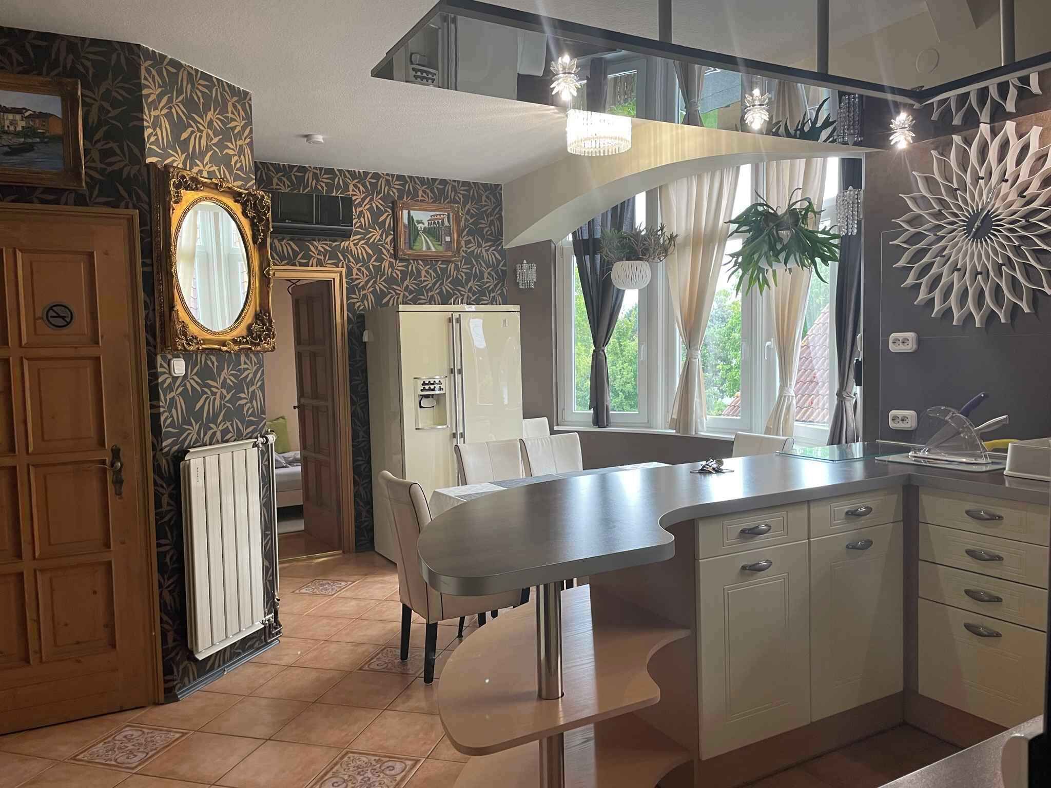 A modern kitchen with a curved island, a refrigerator, and a dining area with chairs.