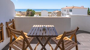Ein Holztisch und Stühle auf einem Balkon mit Blick auf das Meer und Gebäude.