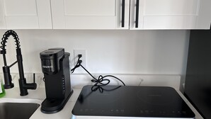 Une cuisine équipée d’une machine à café, d’une bouilloire et d’une plaque de cuisson à induction.