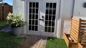 Une maison blanche avec une porte à deux battants, un pot de fleurs et un banc en bois.