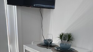 Une table à manger blanche avec deux chaises, un téléviseur fixé au mur et une plante en pot posée sur la table.