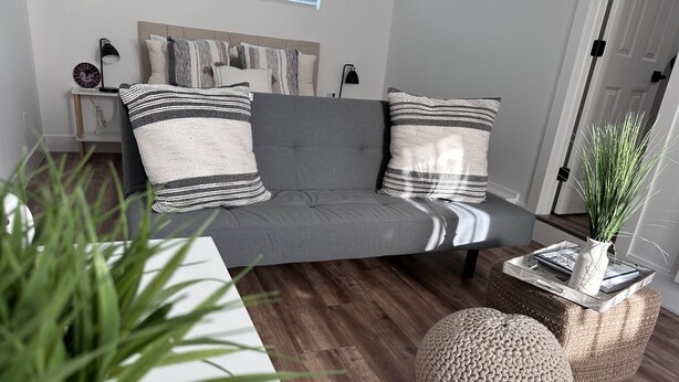 Un salon moderne avec un canapé gris, des coussins à rayures, une table basse blanche et deux poufs ronds.