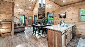 Interior espacioso de una cabaña de madera con comedor, cocina y una sala de estar acogedora.