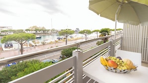 A balcony with a table holding a fruit basket, overlooking a marina with boats and trees. - Holiday apartment mit Klimaanlage und Terrasse (Lignano)