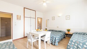 A room with a white table, two beds with matching blue floral bedding, a ceiling fan, and a small plant on a nightstand. - Holiday apartment mit Klimaanlage und Terrasse (Lignano)