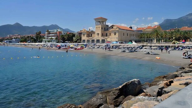 Uma vila costeira com um edifício imponente, uma praia de areia e um litoral rochoso.