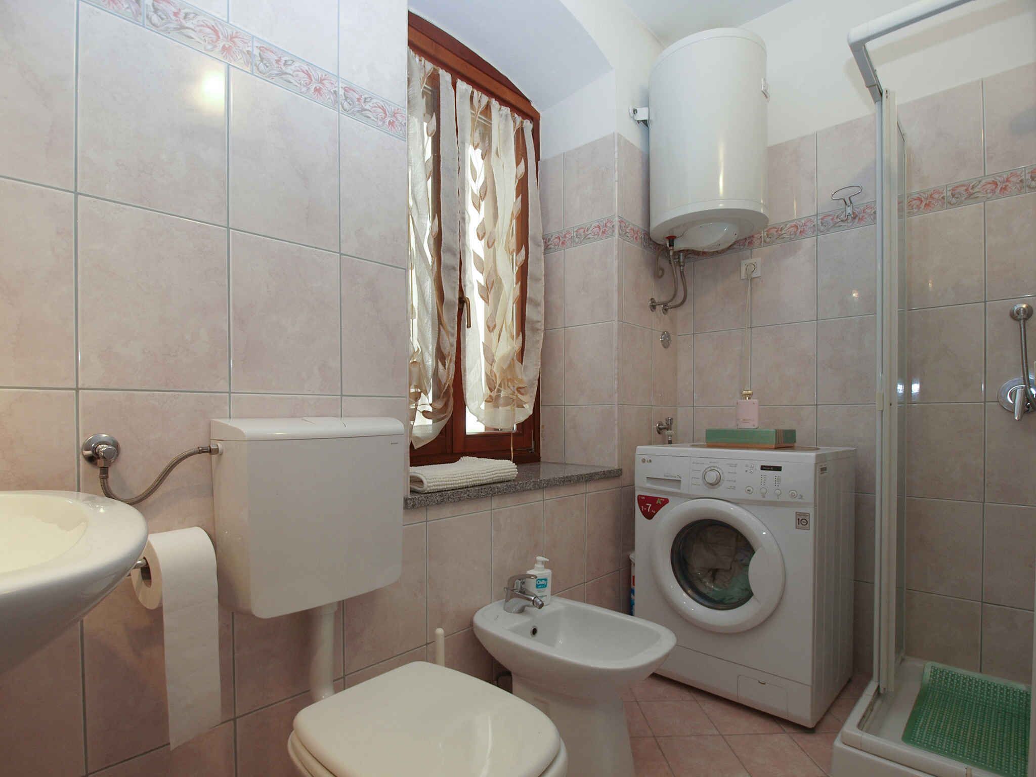 A bathroom with a toilet, sink, bidet, washing machine, and shower.