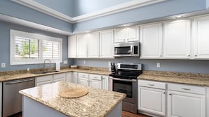 A modern kitchen with white cabinets, granite countertops, a built-in microwave, and a large island with a woven placemat. - "Peaceful Avondale Escape – Pool, Hot Tub, Outdoor Living!" (Avondale)