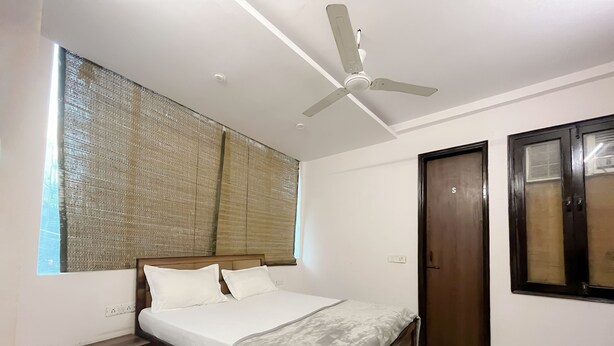 Ein Schlafzimmer mit einem Bett, einem Nachttisch, einem Deckenventilator und einem großen Fenster mit Jalousien.