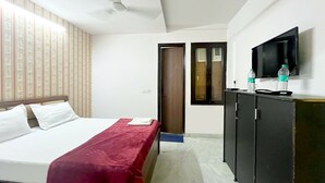 Ein Hotelzimmer mit einem Bett, einer roten Tagesdecke, einem Deckenventilator, einem Fernseher und einem Schrank mit Wasserflaschen.