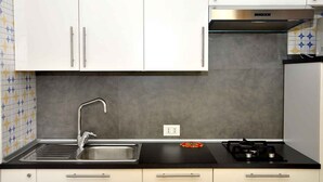 Una cucina con mobili bianchi, un lavello in acciaio inossidabile, un fornello a gas e un rivestimento murale decorato.