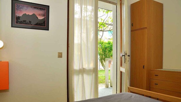 Una camera da letto con un letto, un armadio in legno, una porta che dà sull'esterno e un quadro appeso al muro.